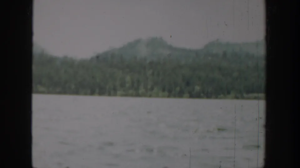 1940 Washington 8mm view of rippled water, forested hills, and soft mountains seen through a dark frame edge.