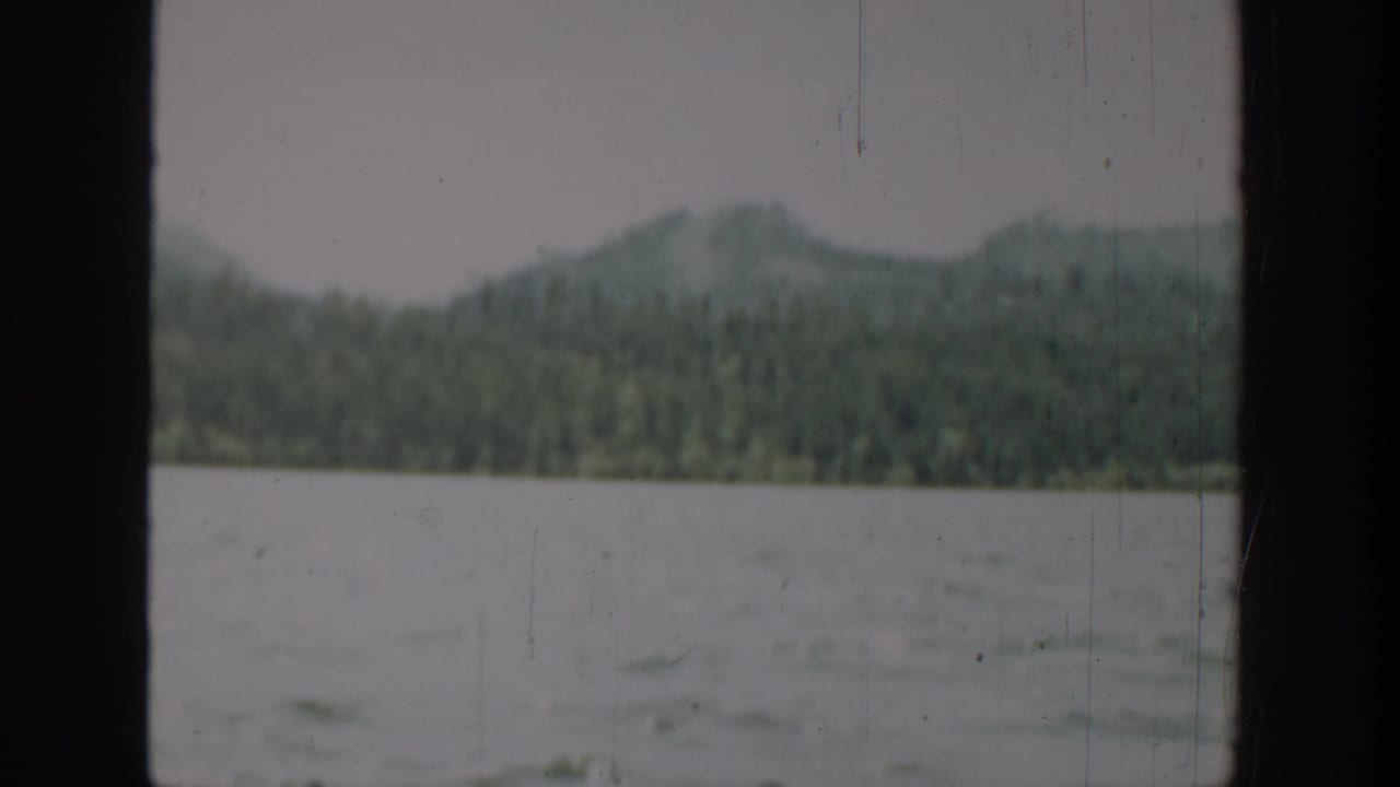 1940 Washington 8mm landscape with rippled water, evergreen shoreline, distant hills, and dark vertical window framing.