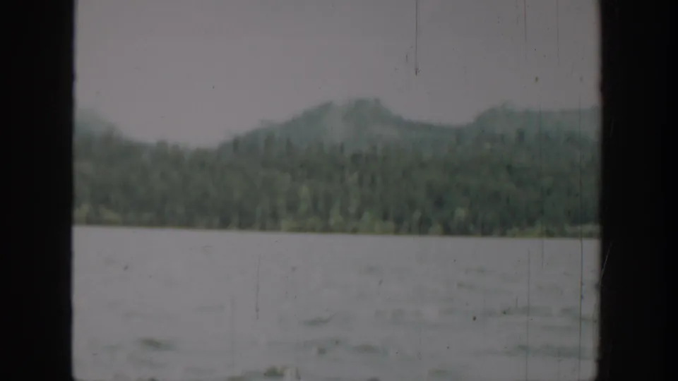 1940 Washington 8mm landscape with rippled water, evergreen shoreline, distant hills, and dark vertical window framing.