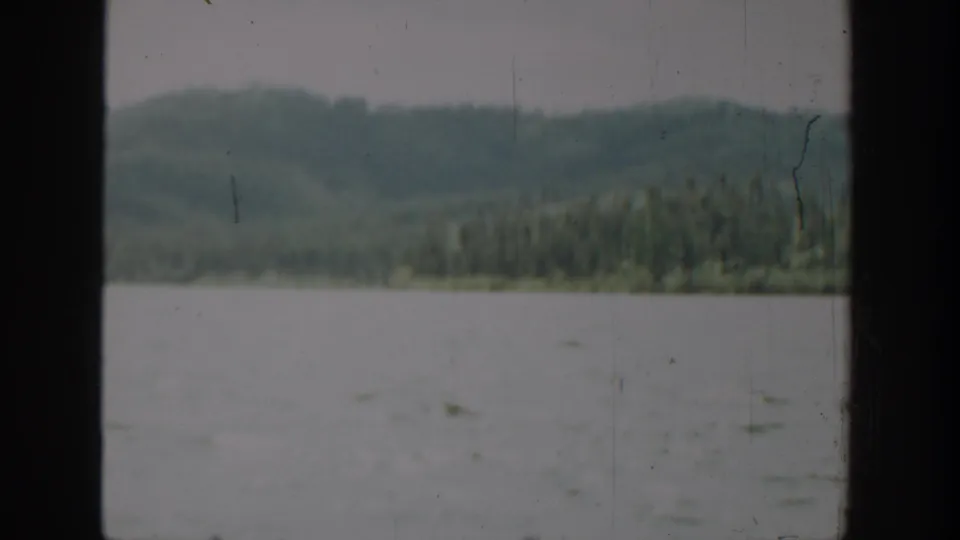 1940 Washington 8mm frame showing pale rippled water, evergreen shoreline, low hills, and dark window borders.