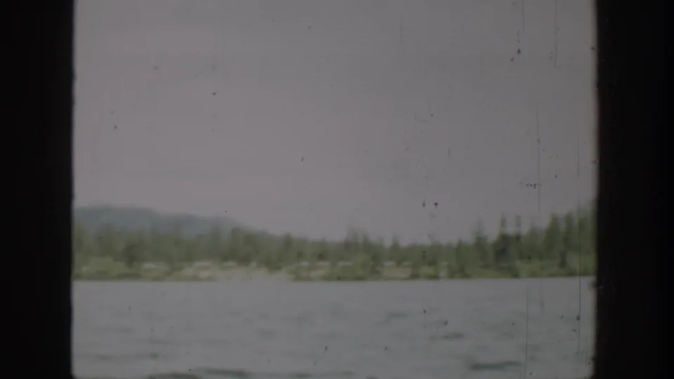 1940 Washington 8mm view of open water, low evergreen shoreline, hazy hills, and pale overcast sky.