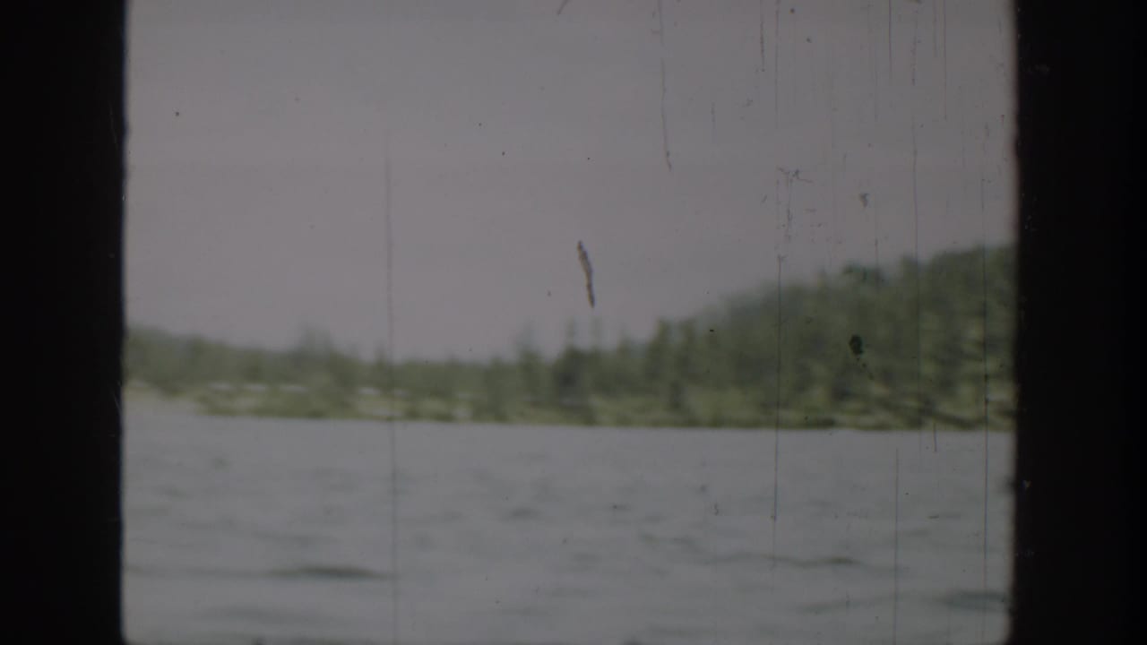 1940 Washington home-movie frame showing lake water, distant tree-lined shore, low hills, and dark film-frame edges.