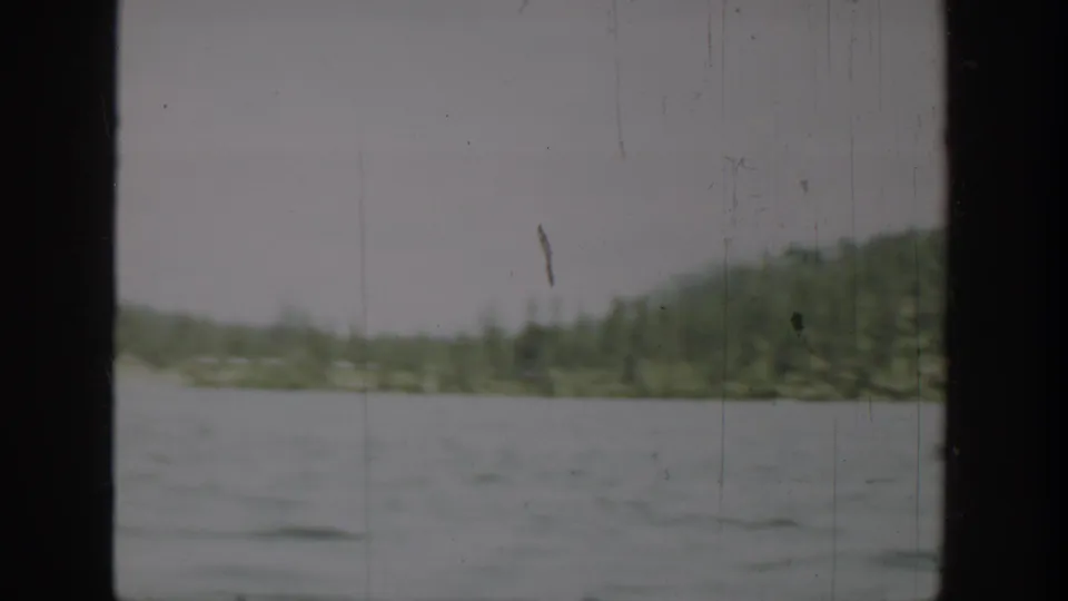 1940 Washington home-movie frame showing lake water, distant tree-lined shore, low hills, and dark film-frame edges.