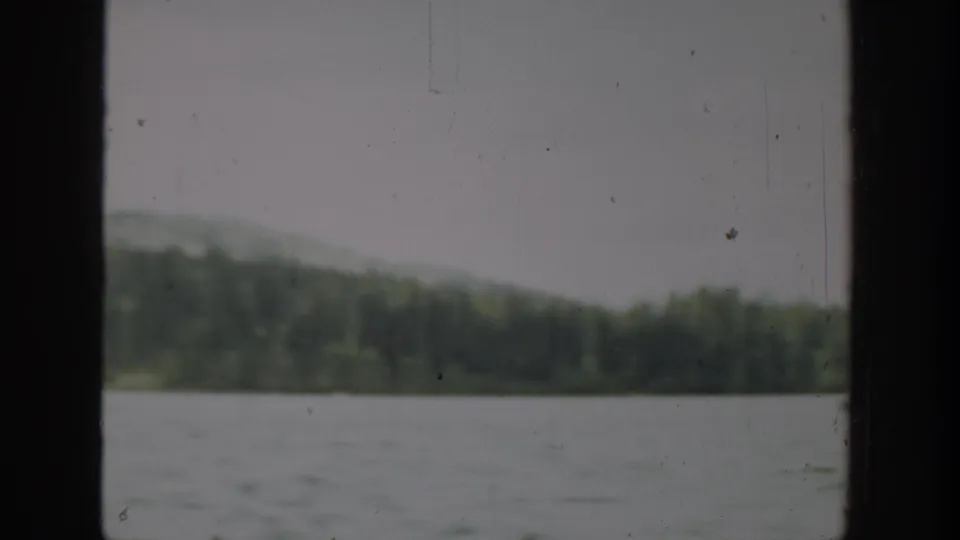 1940 Washington home-movie frame showing a soft, slightly blurred lake view with forested hills and physical film marks.