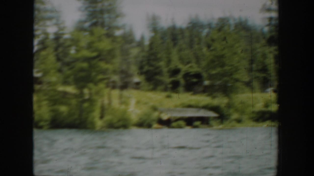 1940 Washington home-movie view of evergreen shoreline, cabins, and lake water filmed from a moving boat.