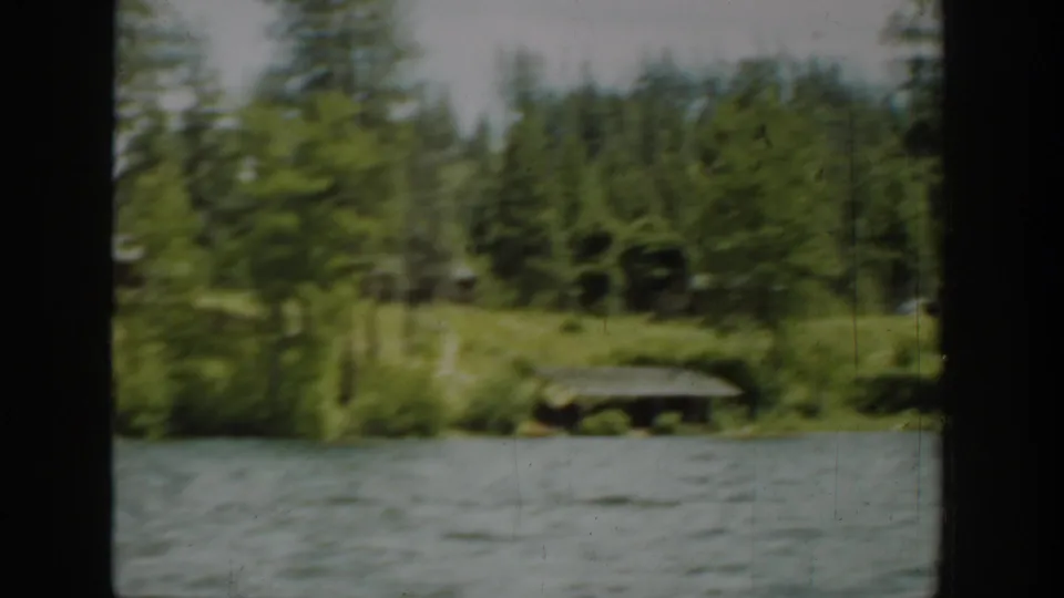 1940 Washington home-movie view of evergreen shoreline, cabins, and lake water filmed from a moving boat.
