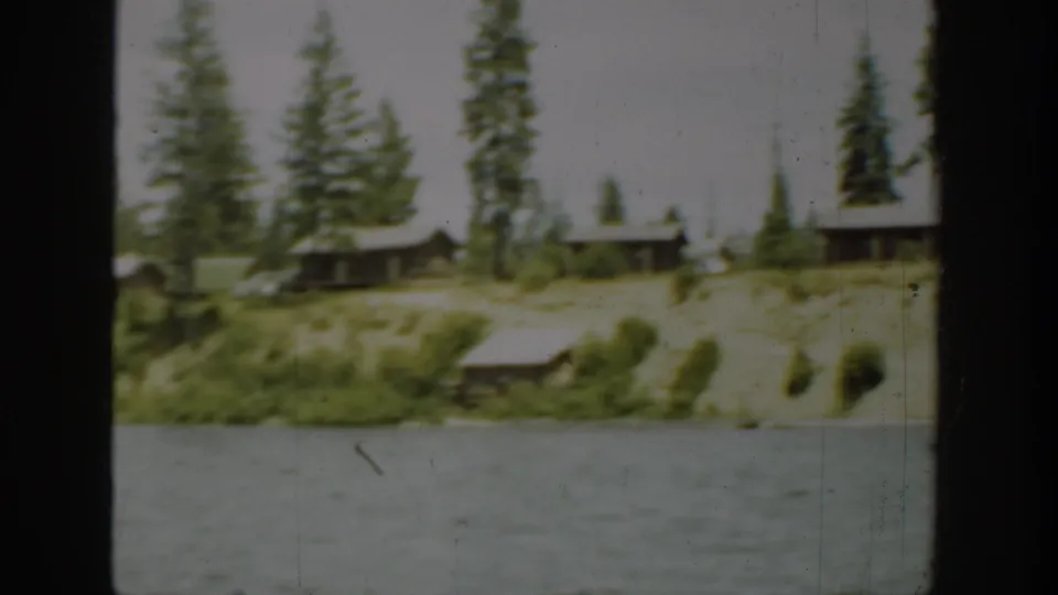 1940 Washington home-movie frame showing cabins, evergreen trees, shoreline brush, and lake water.