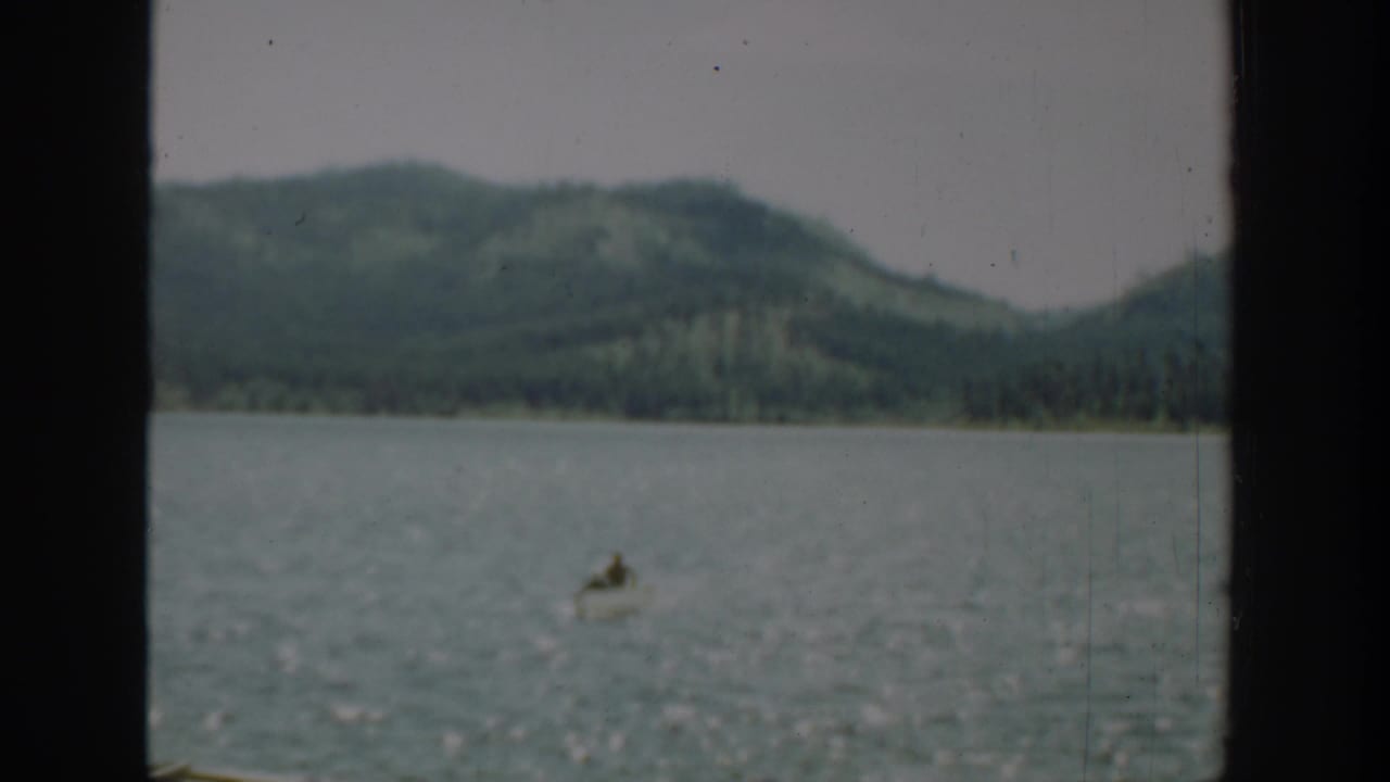 Distant small boat on open water with wooded hills behind it.