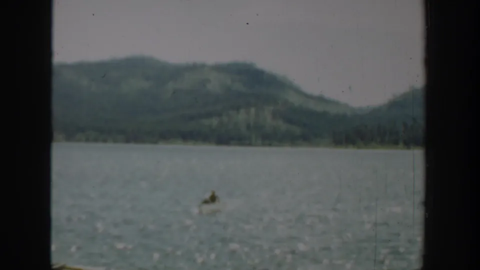 A small boat appears far out on a Washington lake in this 1940 8mm frame, with forested hills and a dark window divider visible.