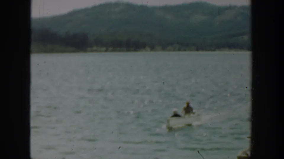 The small boat with two occupants continues across the lake in Washington, with rippled water and wooded hills visible in the 1940 8mm frame.