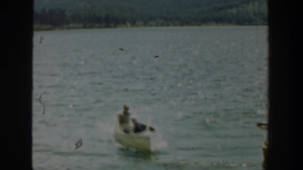 Two people in a small white rowboat on a lake, framed by dark film borders.