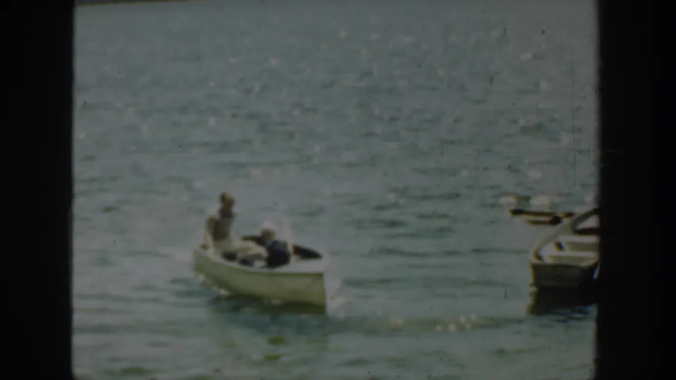 The rowboat continues across the lake, with docked boats partly visible along the right side of the frame.