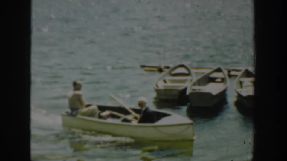 The two-person rowboat passes a cluster of docked boats in soft, faded 8mm footage from Washington.