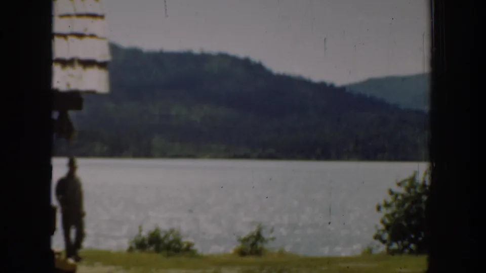 Washington 1940 8mm frame with a man in military-style attire near a bright lake and forested hills.