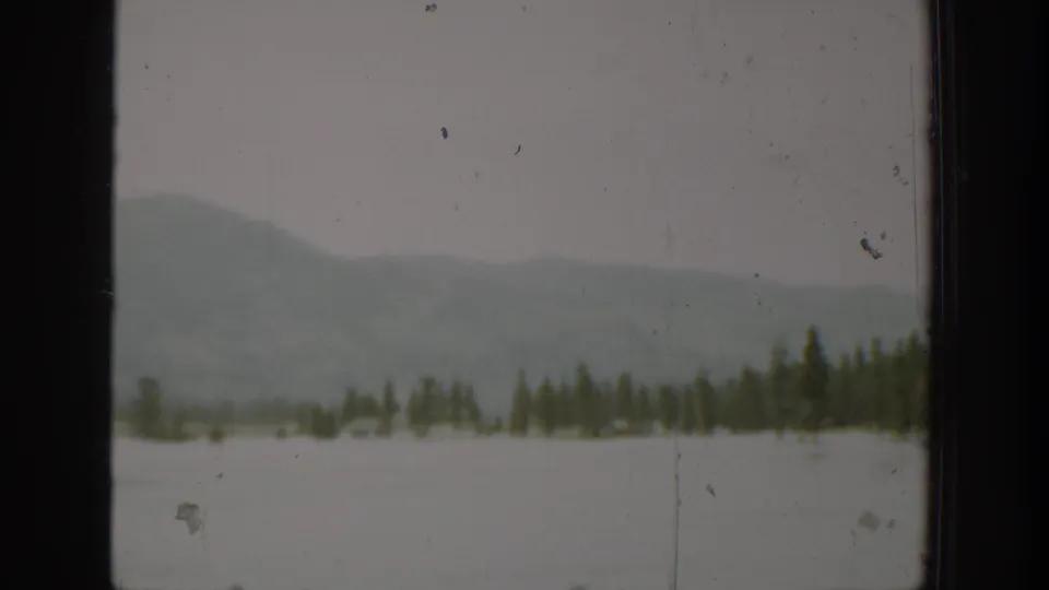 1940 Washington 8mm frame showing pale water, a low evergreen shore, and soft misty hills beyond a dark window edge.