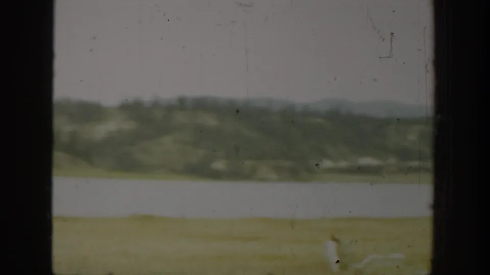 Muted home-movie landscape in Washington with grass, water, distant hills, and a hazy tree line.