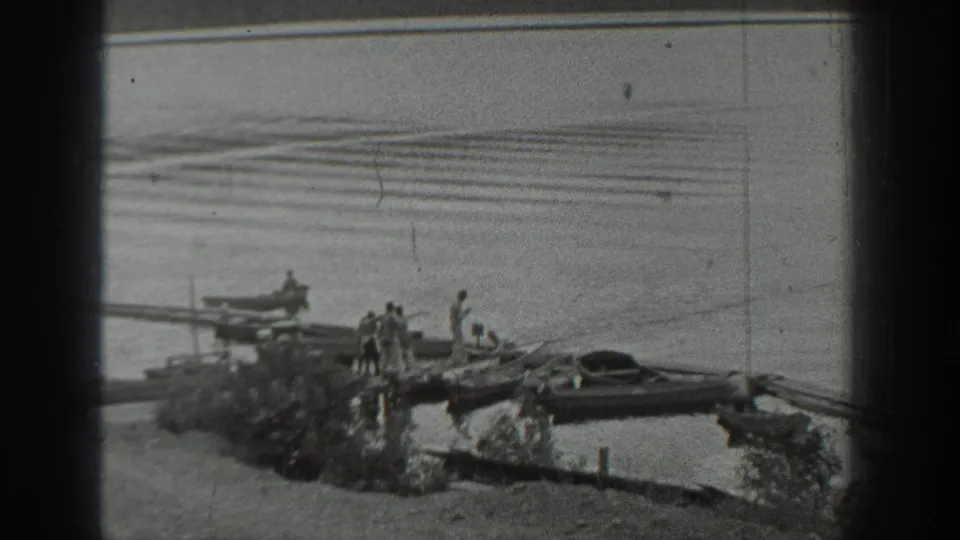 Several people gather on a lakeside dock in Washington while small boats sit at the shore and a rowboat rests on calm water.
