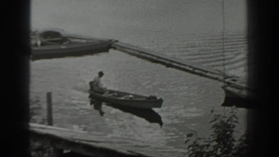 In Washington archival 8mm footage from 1940, a man sits alone in a small boat on rippled lake water near a dock.