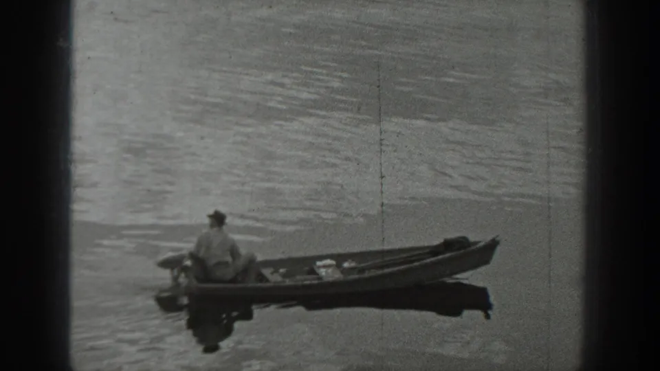 At the end of the clip, the man sits alone in the small boat on open rippled lake water, with no clear landmark visible.