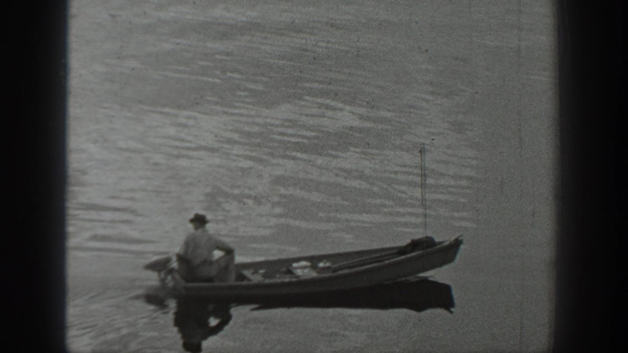 1940 Washington home-movie frame showing a man in a cap seated in a canoe on a calm lake with ripples around the boat.