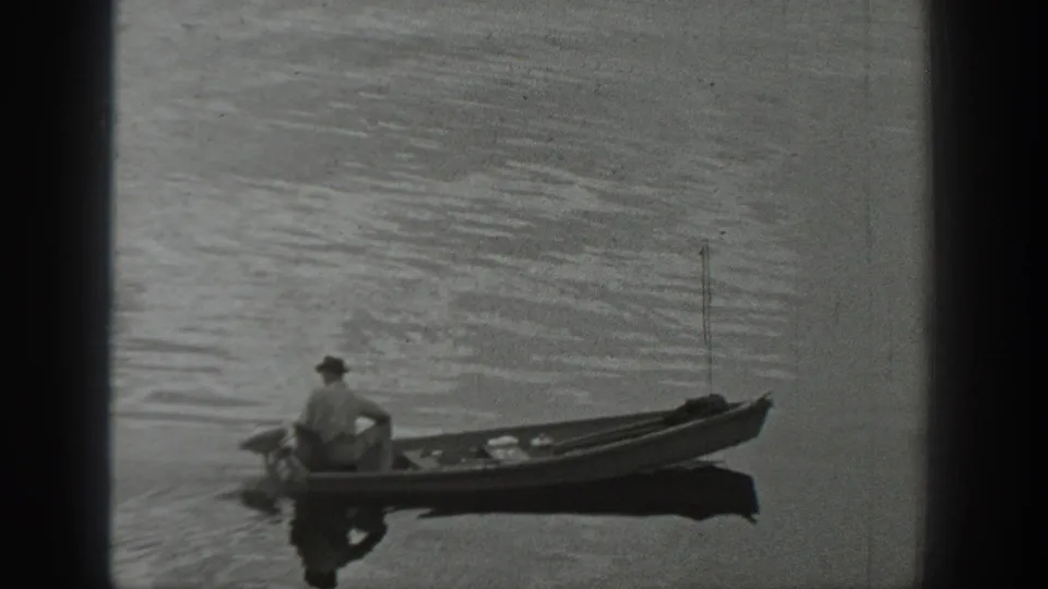 1940 Washington home-movie frame showing a man in a cap seated in a canoe on a calm lake with ripples around the boat.
