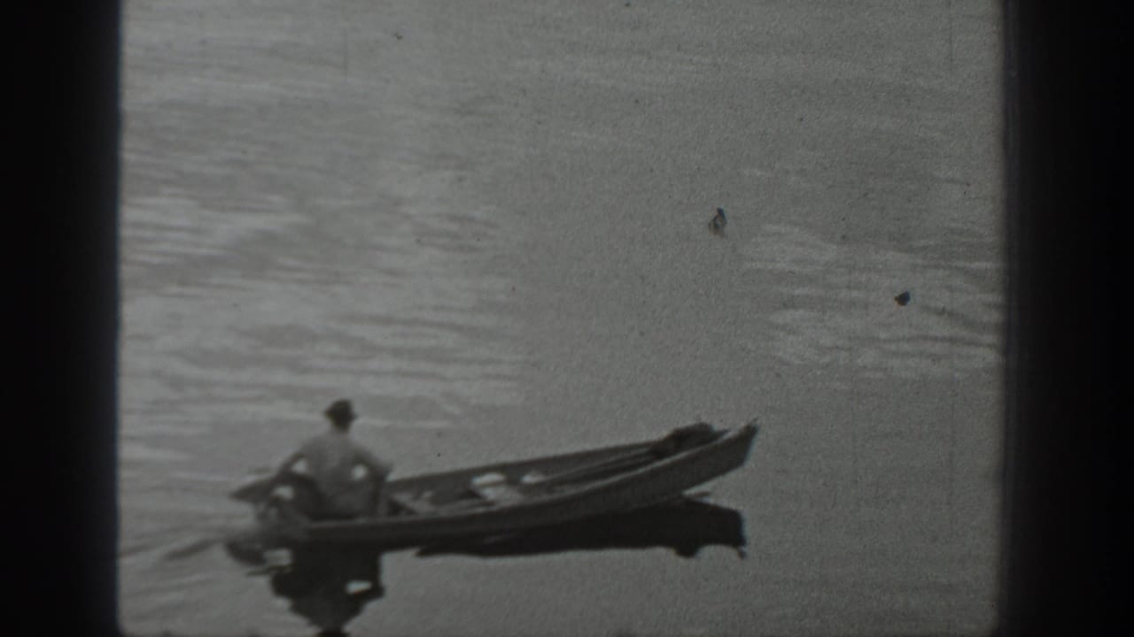 Black-and-white 8mm frame of a distant man paddling a canoe across a Washington lake, with soft focus and visible film borders.