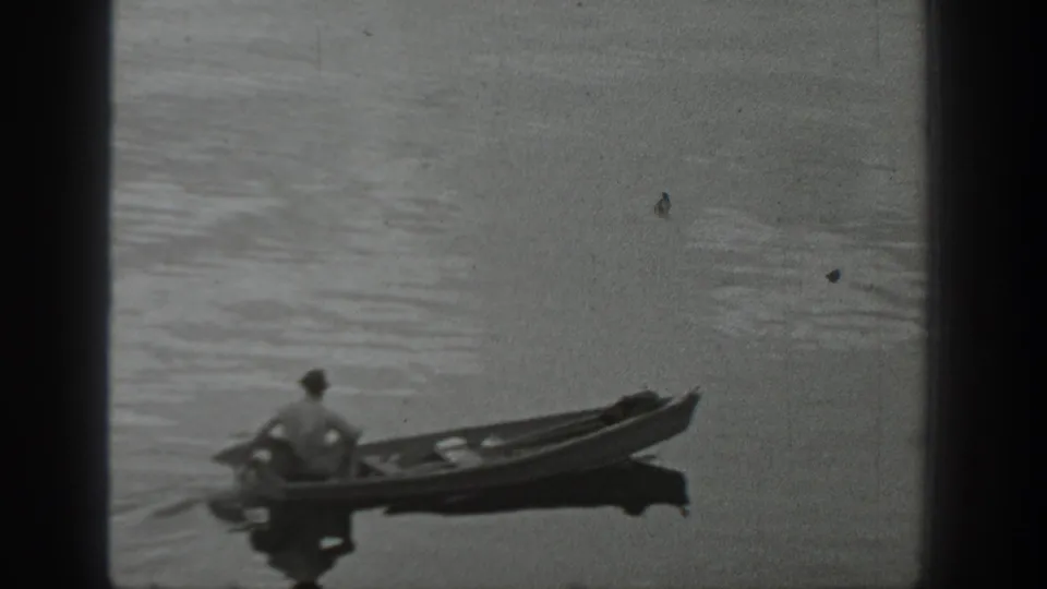 Black-and-white 8mm frame of a distant man paddling a canoe across a Washington lake, with soft focus and visible film borders.