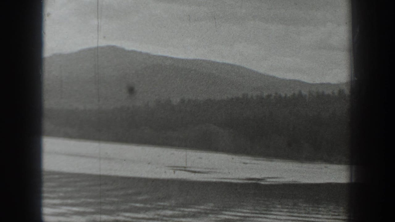 Black-and-white 8mm view of a Washington mountain lake with forested shoreline and hills, partly obscured by dark frame bars.