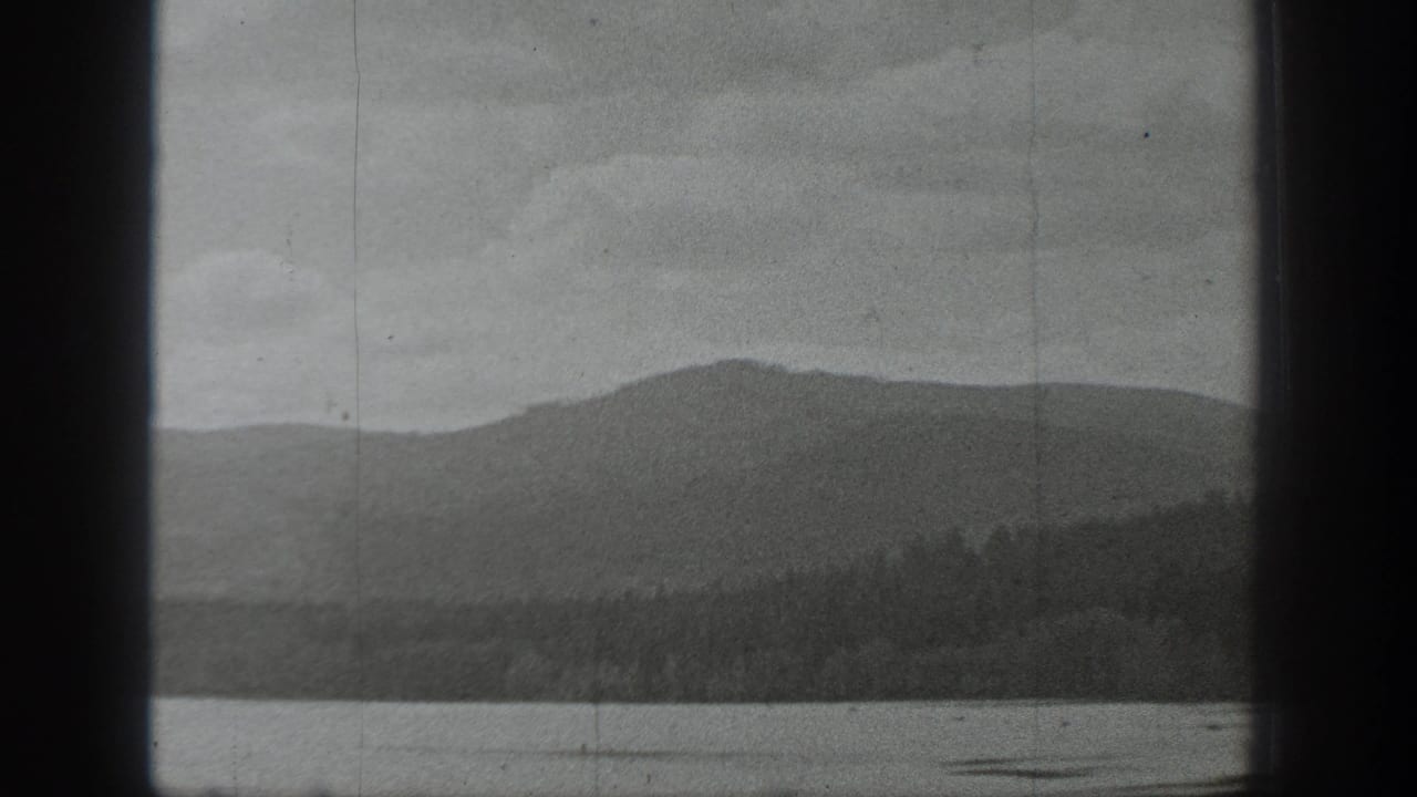 Black-and-white Washington lake view showing calm water, a wooded shoreline, and low mountains in the distance.