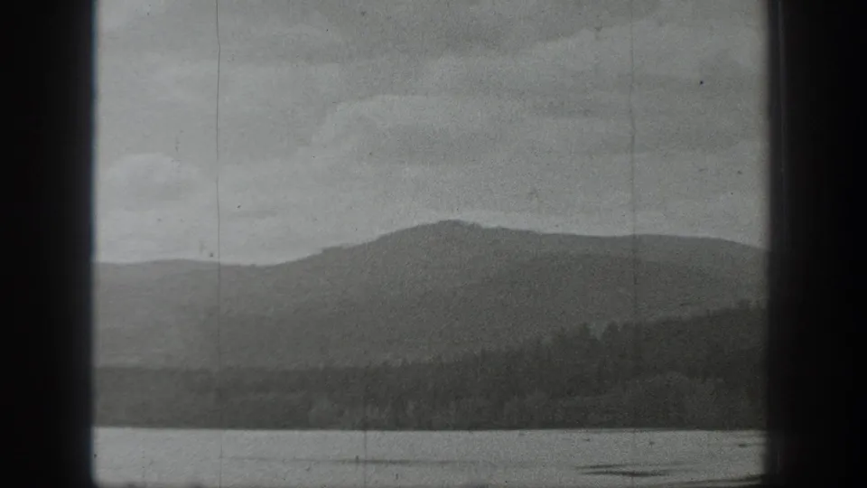 Black-and-white Washington lake view showing calm water, a wooded shoreline, and low mountains in the distance.