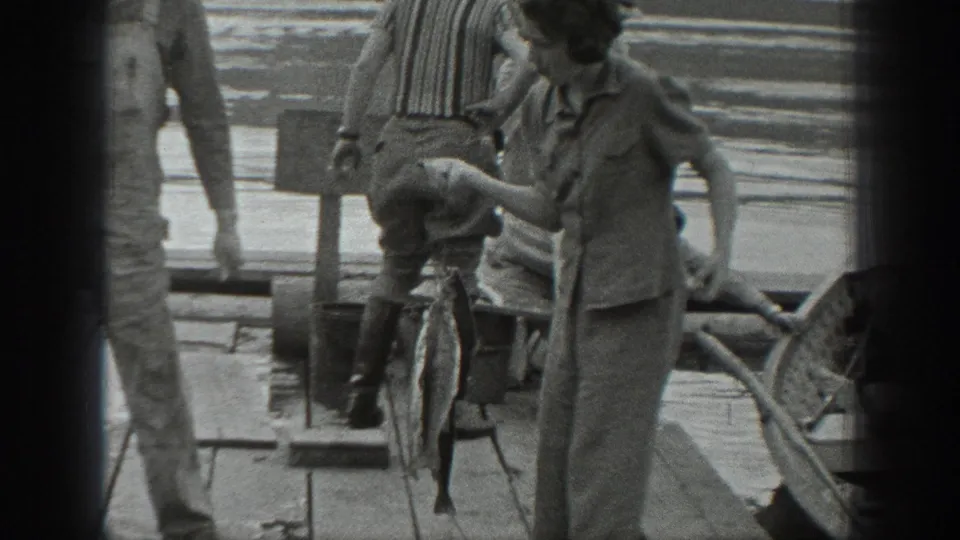 1940s Washington lakeside pier scene with a woman holding a caught fish, another person nearby, and a striped umbrella behind her.