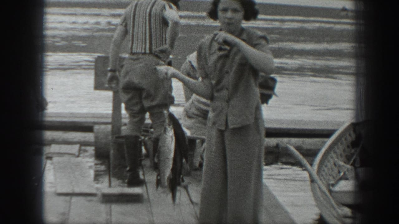 In 1940 Washington home-movie footage, a woman stands on a dock with a large fish beside a striped-shirted man near lake water.