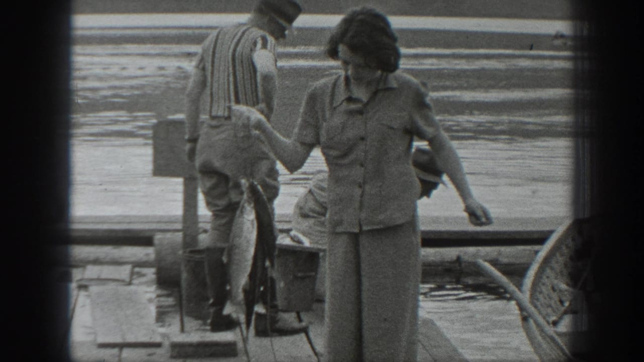 Woman on a wooden dock looks down while holding or gesturing near a hanging fish.