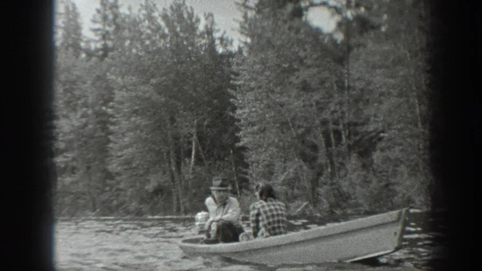 Two people, including a hat-wearing man, sit in a small motorboat on a forested Washington lake in 1940 black-and-white 8mm footage.