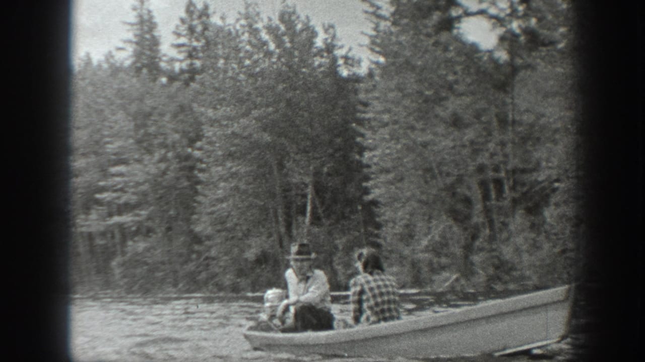 1940 Washington 8mm frame of a couple in a small motorboat beside evergreen trees on a lake.
