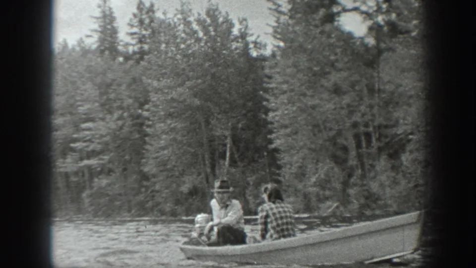 1940 Washington 8mm frame of a couple in a small motorboat beside evergreen trees on a lake.