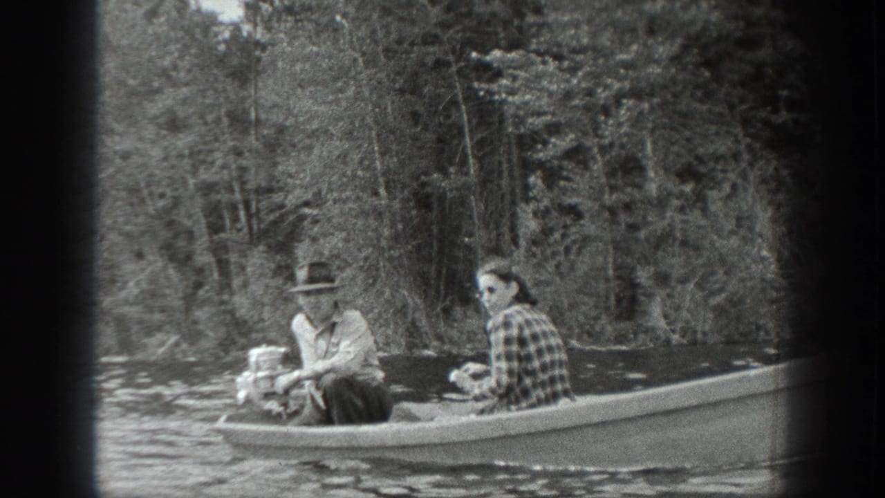 A man and woman sit in a motorboat on calm water with trees behind them.