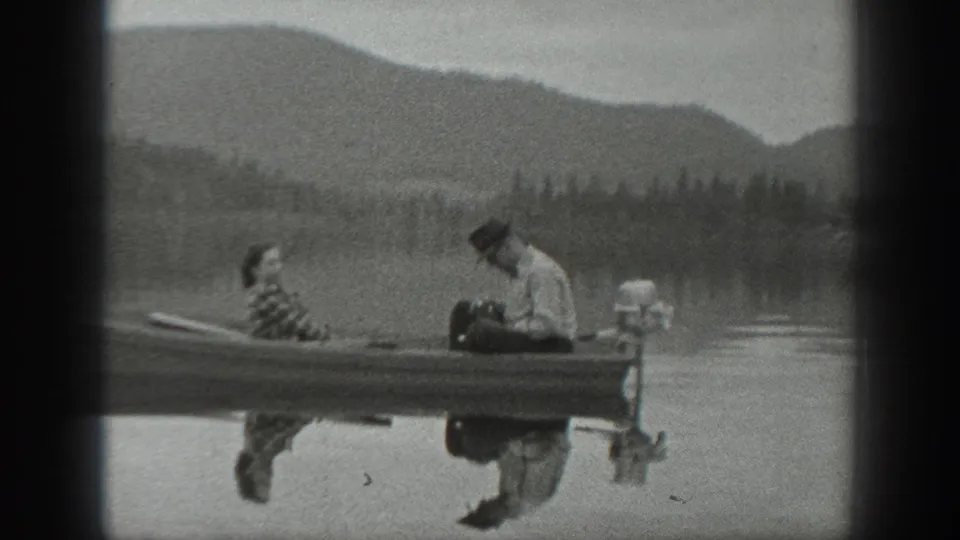 Washington 1940 frame with a man tending a small outboard motor as a woman sits nearby on a lake.