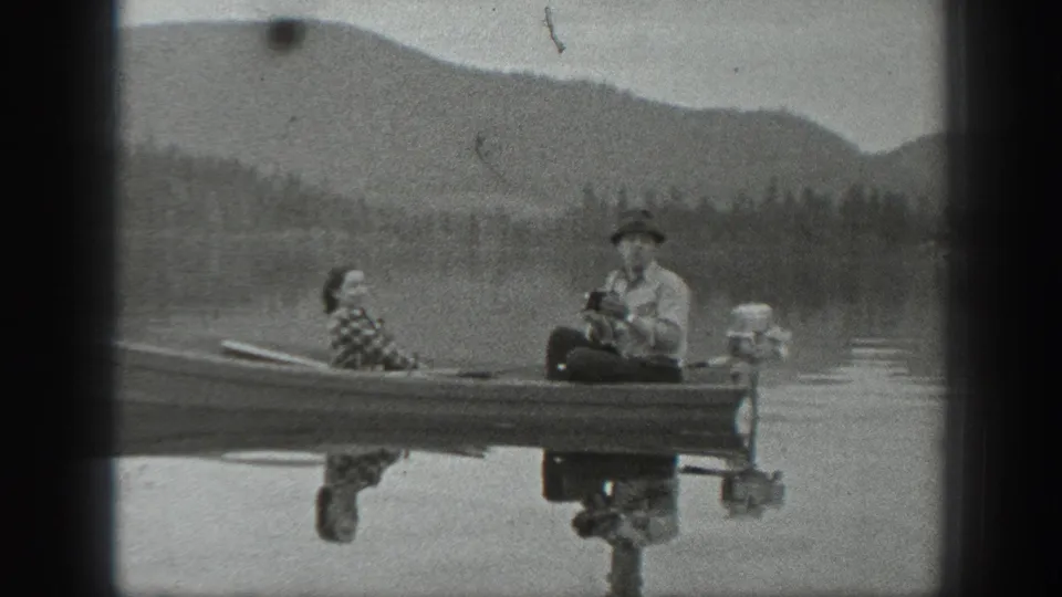 Washington 1940 8mm frame showing two adults in a small motorboat, with the hull reflected in still water.