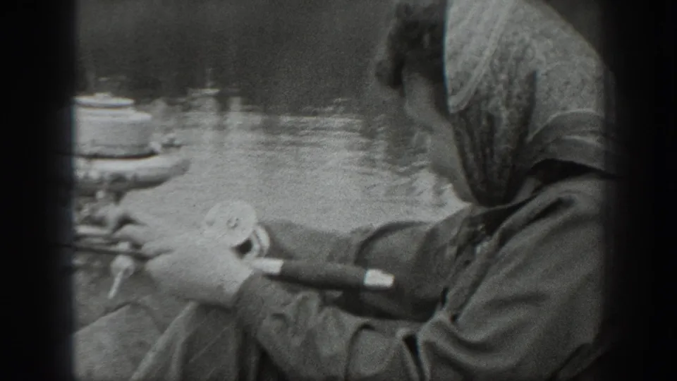 Close Washington 1940 home-movie frame of a woman in a headscarf seated near an outboard motor on a lake.