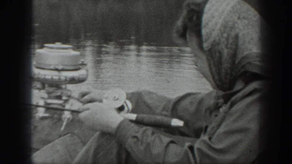 1940 Washington 8mm frame showing a woman in a headscarf and coat fishing from a small boat on a calm lake.