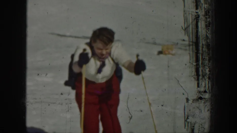 A closer 1940 home-movie view shows the skier in red pants and dark gloves moving past the camera on snow.