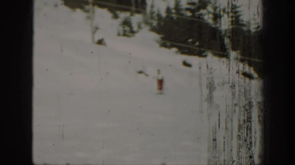 A distant skier appears on a wide snowy slope in Washington, with evergreens and aged 8mm film wear visible.