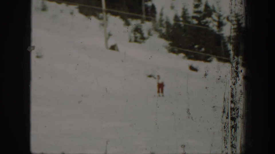 1940 Washington 8mm frame showing a lone cross-country skier on a pale snow slope below dark conifers.