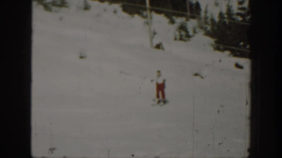1940 Washington 8mm frame showing a distant adult skier in red pants on a snowy hillside below dark trees.