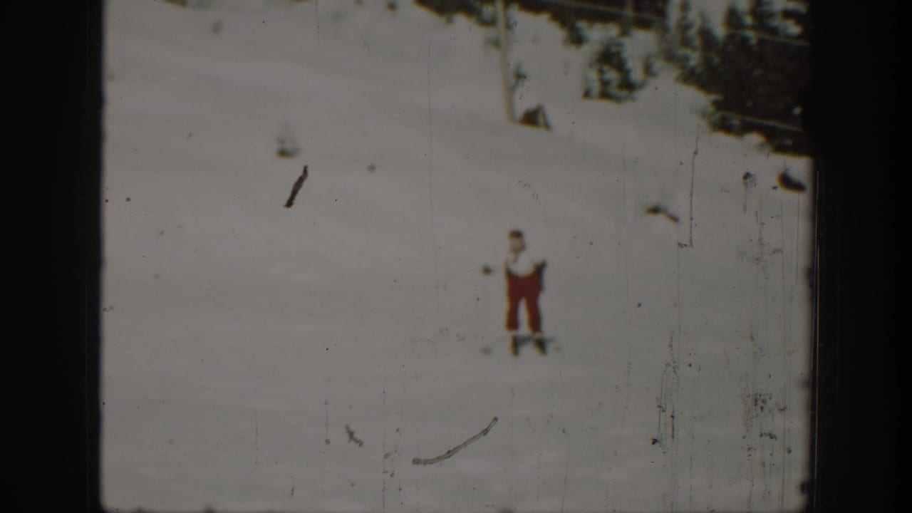 Small skier in red pants moves across a bright snowy hillside.