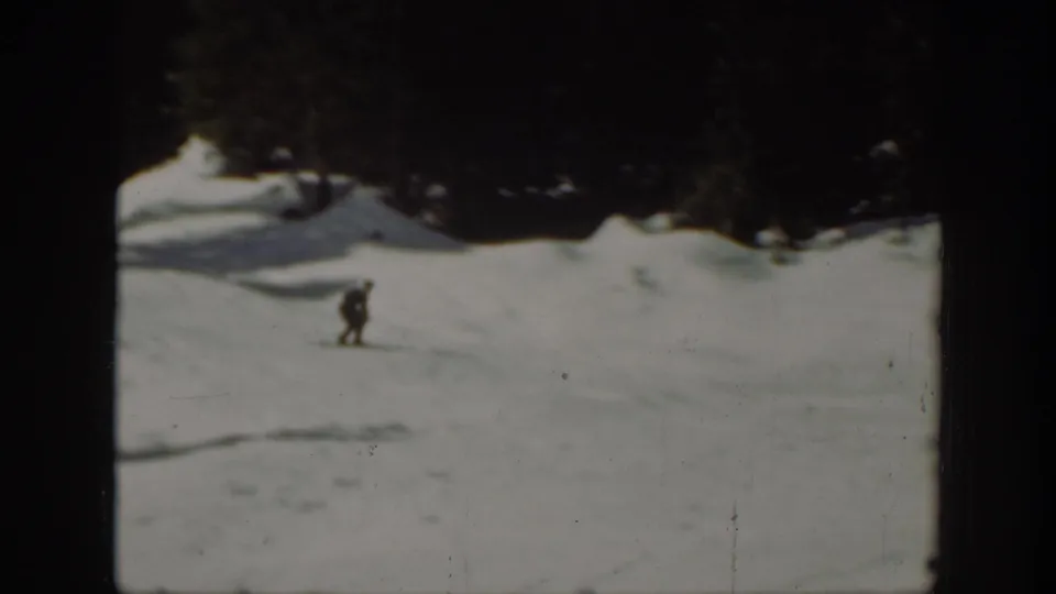 1940 home-movie view of a distant skier crossing an open snowy practice area in Washington, with dark trees beyond.