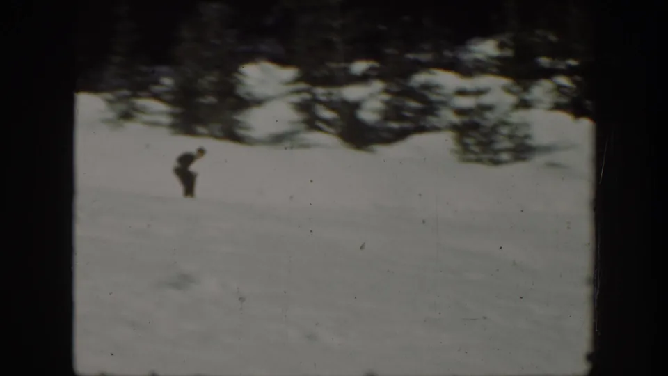 A distant skier in dark clothing stands or moves on a snow-covered Washington hillside in 1940s 8mm home-movie footage.