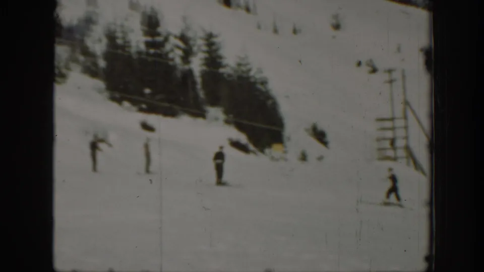 Distant skiers move or stand on a snowy slope near lift poles and a small structure, consistent with a developing ski area.