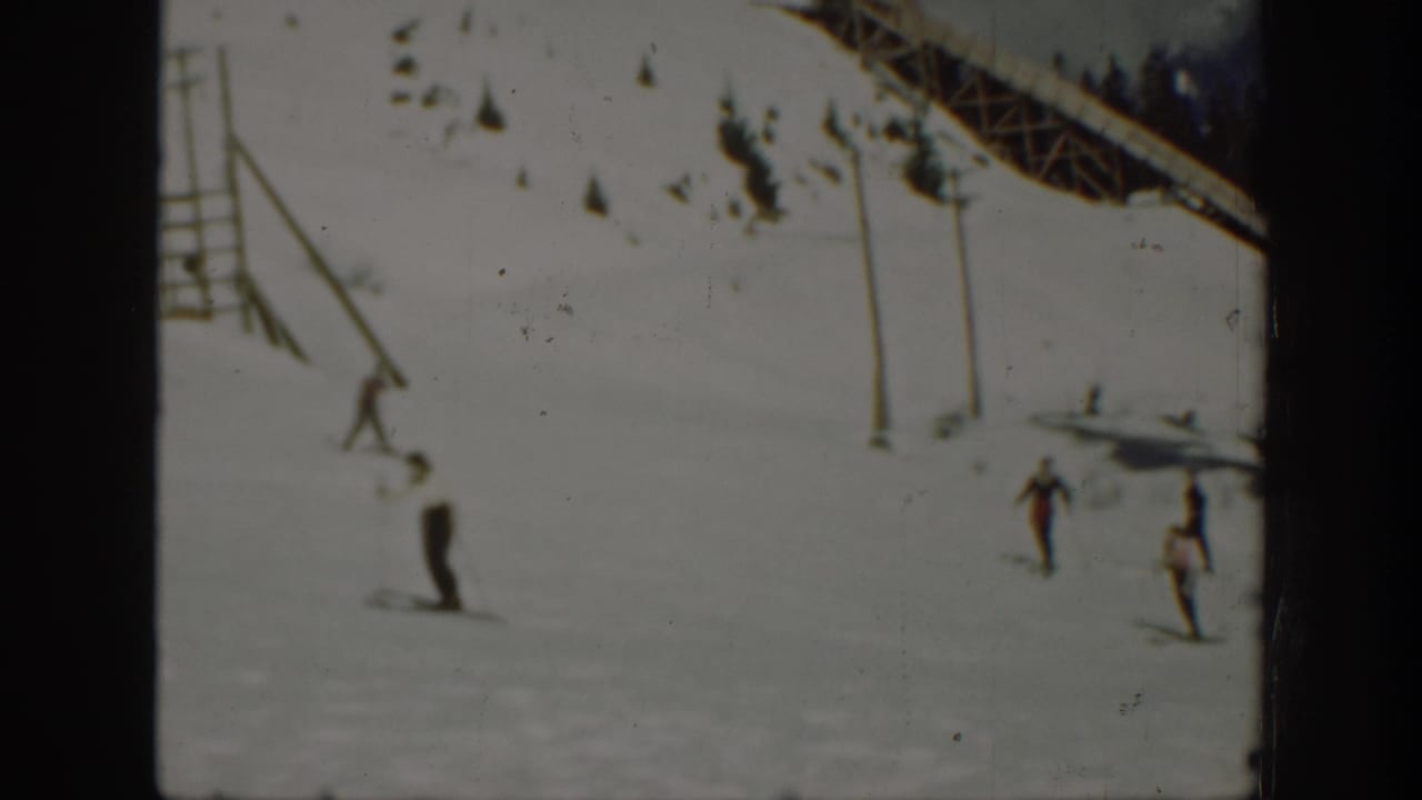 1940 Washington home-movie frame showing distant skiers moving down a snowy slope beneath a lift or trestle structure.